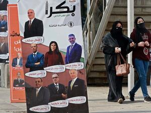 Women, mask-clad due to the COVID-19 coronavirus pandemic, walk past a campaign banner for an electoral list running in the general election scheduled for the following day, along a street in Jordan's capital Amman on November 9, 2020. Voters in coronavirus-battered Jordan go to the polls on November 10 in an election focused on the Arab country's economic crisis which has been heightened by the devastating pandemic. Although there have been some calls on social media to postpone the elections, the governme