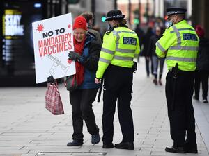 A protestor holding a placard is spoken to by police officers as she attends an anti-vaccine demonstration outside the offices of the Bill and Melinda Gates foundation in central London on November 24, 2020. British Prime Minister Boris Johnson told MPs that thanks to a potential vaccine "the escape route is in sight" from the coronavirus crisis -- while warning that in the immediate future "Christmas cannot be normal". JUSTIN TALLIS / AFP