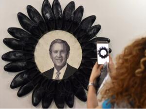 A visitor takes a picture of George W. Bush surrounded by black shoes during the opening of the Beirut Art Fair (Twitter)