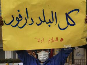 In this file photo taken on July 4, 2020, A mask-clad demonstrator (due to the COVID-19 coronavirus pandemic) stands with a sign reading in Arabic "all of the country is Darfur, #PeaceFirst", during a protest outside the Sudanese Professionals Association in the Garden City district of Sudan's capital Khartoum, in solidarity with the people of the Nertiti region of Central Darfur province in the country's southwest. ASHRAF SHAZLY / AFP