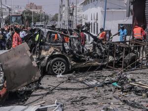 Rescue personnel and bystanders gather near debris at the site of a suicide car bombing attack near a security checkpoint in Mogadishu on February 13, 2021. Three people were killed and eight wounded after a car bomb detonated near a security checkpoint in the Somali capital Mogadishu, a security official and witnesses said. Abdirazak Hussein FARAH / AFP