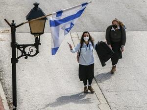 Israeli schoolgirls, clad in mask due to the COVID-19 coronavirus pandemic, walk underneath an Israeli flag hanging from a lamp post along al-Shuhada street, largely closed to Palestinians, in the city centre of the flashpoint city of Hebron in the occupied West Bank on February 21, 2020. HAZEM BADER / AFP
