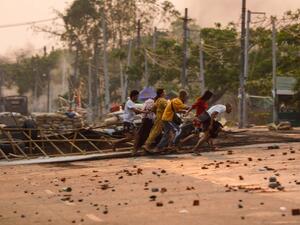 People run past makeshift barricades set up by protesters, during a crackdown by security forces on demonstrations against the military coup, in Hlaing Tharyar township in Yangon on March 14, 2021. STR / AFP People run past makeshift barricades