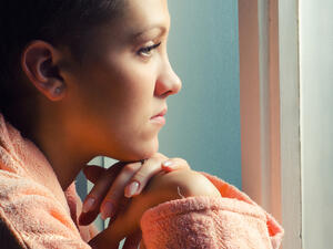Young depressed cancer patient standing in front of hospital window