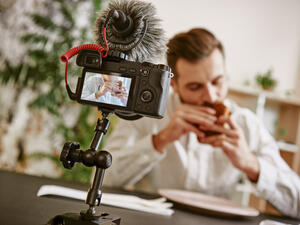 Close up of digital camera screen with male food blogger eating a sandwich while recording video for his vlog.