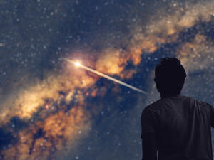 Man observing the night sky and Milky way with a shooting star trail