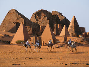 Unidentified Sudanese bedouins ride camels with the famous Meroe pyramids of the ancient Nubian city in the background, on November 02, 2007 in Sudan