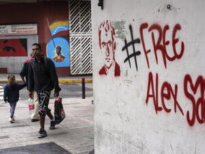 People walk near a graffiti demanding Colombian businessman Alex Saab's freedom, in Caracas, on February 23, 2021. Saab, who is allegedly close to Venezuelan President Nicolas Maduro and wanted in the US for money laundering, has been put under house arrest in Cape Verde. Saab was detained in June 2020 as a plane he was travelling on stopped over in the African country. / AFP / Yuri CORTEZ Barlavento Court, concerned about Alex Saab declining health, initiates immediate transfer to capital city, Praia.