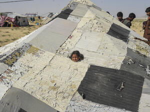 A child peeps out from a ruptured area of a tent as other Afghan refugees talk among themselves at a temporary settlement on the outskirts of Quetta on September 6, 2021. (Photo by Banaras KHAN / AFP) Comprehensive Refugee Resettlement Program Urgently Needed
