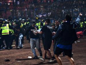 In this picture taken on October 1, 2022, a group of people carry a man after a football match between Arema FC and Persebaya Surabaya at Kanjuruhan stadium in Malang, East Java. At least 127 people died at a football stadium in Indonesia late on October 1 when fans invaded the pitch and police responded with tear gas, triggering a stampede, officials said. (Photo by AFP)