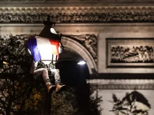 A football fan, sitting on a lamp post next to the Arc de Triomphe, celebrates after France's victory over Morocco in the Qatar 2022 World Cup semi-final, on the Champs-Elysees in Paris on December 14, 2022. (Photo by Thibaud MORITZ / AFP)