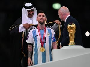 Qatar's Emir Sheikh Tamim bin Hamad al-Thani (L) wraps an abaya around Argentina's forward #10 Lionel Messi on stage next to the FIFA World Cup Trophy after Argentina won the Qatar 2022 World Cup final football match between Argentina and France at Lusail Stadium in Lusail, north of Doha on December 18, 2022. (Photo by Paul ELLIS / AFP)