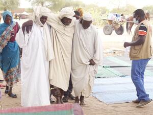 رجلان يساعدان لاجئًا سودانيًا مسنًا عبر الحدود إلى تشاد في مخيم في الكفرون 
