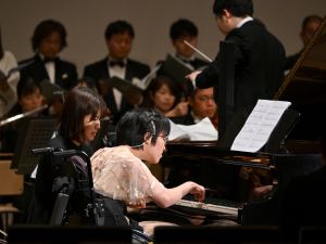 Kiwa Usami (C), who has cerebral palsy and performs with one index finger, playing an AI-powered piano during a Christmas concert rehearsal. (Photo by Kazuhiro NOGI / AFP) piano