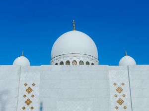 واجهة مسجد بقباب بيضاء بارزة تحت سماء زرقاء صافية، في صورة تعبيرية عن دور العبادة الإسلامية.