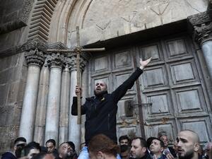 A Palestinian man holds a cross during a protest in front of the Church of the Holy Sepulchre in Jerusalem (AFP/File Photo)