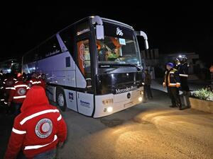 Members of the Syrian Red Crescent and Civil Defence stand by as a convoy of buses carrying rebel fighters and civilians from the Eastern Ghouta enclave town of Harasta arrives in the town of Qalaat al-Madiq, about 45 kilometres northwest of the central city of Hama, early on Mar. 23, 2018. 
(OMAR HAJ KADOUR / AFP)