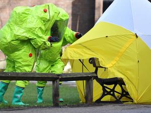 (FILES) In this file photo taken on Mar. 8, 2018 members of the emergency services in green biohazard encapsulated suits afix the tent over the bench where where former Russian spy Sergei Skripal and his daughter Yulia were found on Mar. 4 in critical condition at The Maltings shopping centre in Salisbury, southern England, after the tent became detached. (Ben STANSALL / AFP)