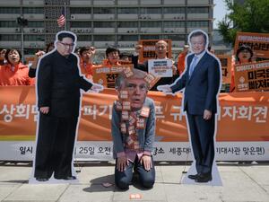 An anti-US protester wearing a face-mask depicting US president Donald Trump (C) kneels between cardboard cutouts of North Korean leader Kim Jong Un (L) and South Korean leader Moon Jae-in (R) (AFP/File Photo)