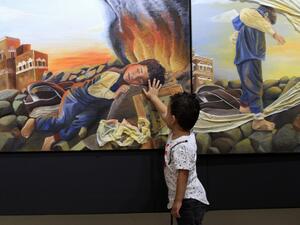 A Yemeni child touches an art work at an art exhibition against war by Yemeni painters at the People's Development Foundation in the Yemeni capital of Sanaa on October 1, 2018 (AFP)