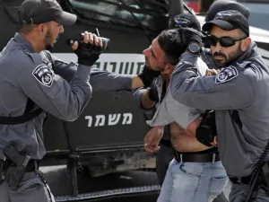 An Israeli policeman films a Palestinian as others hold him as he is being detained during a demonstration at the Palestinian Bedouin village of Khan al-Ahmar (AFP)