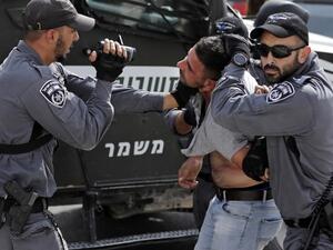 An Israeli policeman films a Palestinian as others hold him as he is being detained during a demonstration at the Palestinian Bedouin village of Khan al-Ahmar (AFP)