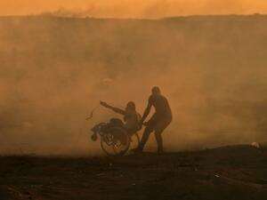 A Palestinian protester pulls a fellow protester on wheelchair amid clouds of tear gas fired by Israeli forces during clashes in east of Gaza City near the Israeli border on November 2, 2018. (MAHMUD HAMS / AFP)