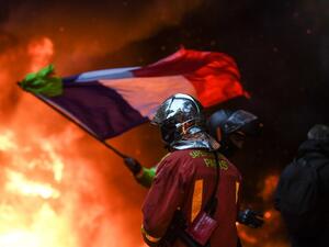 A French fire fighter walks towards flames as a Yellow vests (Gilets jaunes) demonstrator waves the French flag during protests against rising oil prices and living costs in the French capital Paris on December 1, 2018. (AFP)