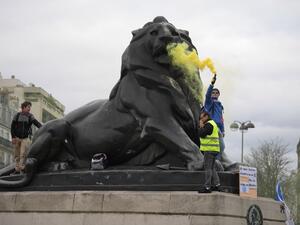 A man holds a flare on the Belfort Lion statue on the Denfert-Rochereau square in Paris, during an anti-government demonstration called by the "Yellow Vest". (Eric FEFERBERG / AFP)
