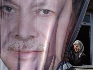 A woman looks from a window partly hidden with a giant poster showing Turkish President Recep Tayyip Erdogan  (AFP)