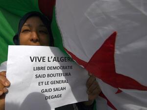 A demonstrator poses with a placard in front of an Algerian flag during a rally in Marseille (AFP)