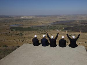 Druze men at the Israeli-annexed Golan Heights flash the V for victory sign as they look out across the southwestern Syrian province of Quneitra, visible across the border (AFP)