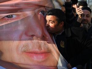 Supporters of ruling Justice and Development Party (AKP) hold a banner picturing Turkish President Recep Tayyip Erdogan while one of them kiss it as they shout slogans during a gathering outside the party's headquarters a day after the local elections (AFP)