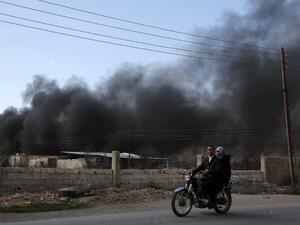 Syrians ride their motorbike as smoke billows in the background following reported air strikes on the rebel-held village of al-Chifouniya, on the outskirts of the capital Damascus, on March 4, 2016. (AFP/Amer Almohibany)