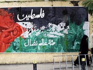 Lebanese people walk past a poster bearing an image of the Palestinian flag and text reading in Arabic: "Palestine, a hundred years of struggle" in Beirut on Dec. 8, 2017 (Joseph Eid/AFP)