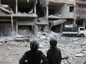 Syrian children look at a building that was damaged in a missile attack on the rebel-held besieged town of Arbin, in the eastern Ghouta region on the outskirts of the capital Damascus, on Jan. 18, 2018 (ABDULMONAM EASSA / AFP)