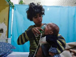 A Syrian boy holds an oxygen mask over the face of an infant at a make-shift hospital following a reported gas attack on the rebel-held besieged town of Douma in the eastern Ghouta region on Jan. 22, 2018 (HASAN MOHAMED / AFP)