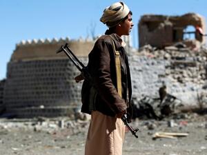 An armed Yemeni youth looks at the debris following a reported air strike in southern Sanaa. (AFP | MOHAMMED HUWAIS)
