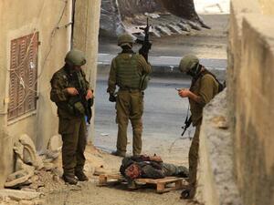 Israeli occupation forces stand over the body of a Palestinian they shot dead in the southern West Bank. (AFP/ File)
