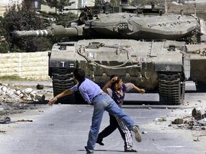 Young Palestinian boys throwing rocks, facing an Israeli tank, (AFP File Photo)