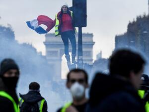 A protestor dressed in yellow vest ("gilets jaunes" in french) holds a french flag as she stands on a red light at the Champs Elysee, in Paris (AFP)