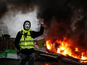 A protester wearing a Guy Fawkes mask makes the victory sign near a burning barricade during a protest of Yellow vests  (AFP)