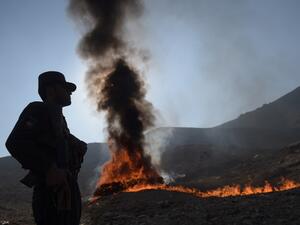 An Afghan policeman watches as a cache of alcohol and drugs burns on the outskirts of Kabul on December 20, 2016. (AFP/Shah Marai)