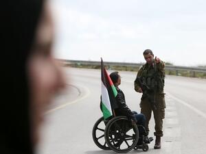 A Palestinian protester on a wheelchair talks with an Israeli soldier during clashes (AFP/file) 