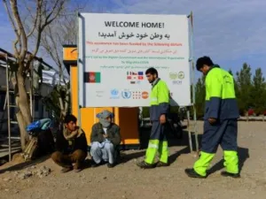 صورة تظهر المهاجرين الأفغان العائدين من إيران لدى جلوسهم تحت لافتة لمنظمة الهجرة الدولية في هرات

