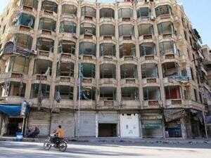 رجل يستقل دراجة نارية بجوار مبنى تعرضت واجهته لدمار في حلب
