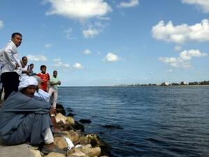 مصريون يجلسون على شاطئ قرية رشيد يراقبون مركبا انطلق في عملية بحث عن عشرات المفقودين في كارثة غرق مركب كان يقل مهاجرين
