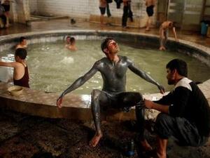 عراقي يغطي ابنه بالرمل من بركة كبريت في حمام العليل
