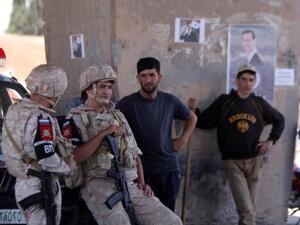 جنديان روسيان يقفان إلى جوار مدنيين خلال افتتاح طريق بين حمص وحماة في الرستن بسوريا
