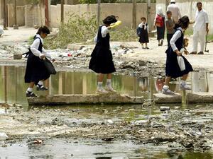 Young school girls cross a trash ridden patch of water on stones in the middle of the road on their way home in Basra. (AFP/ File)